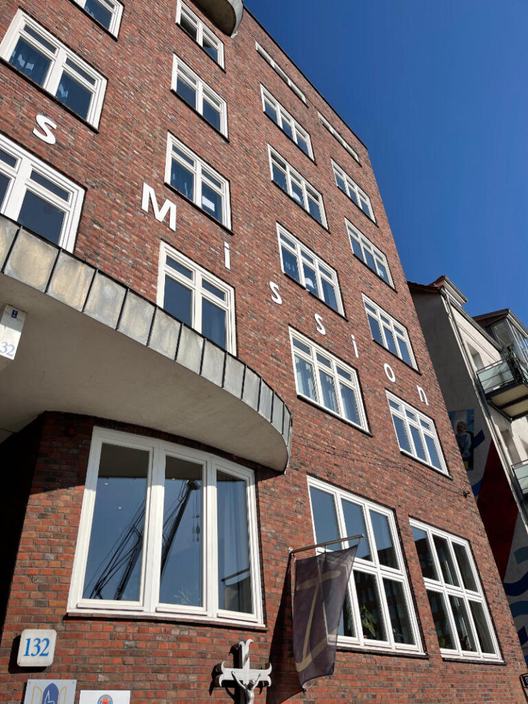 Das Foto zeigt die Deutsche Seemannsmission in Hamburg-Altona, das Seemannshotel an der Großen Elbstraße. Der rote Backsteinbau leuchtet hier in der Sonne eines Sommertages. Der Himmel ist wolkenlos blau.