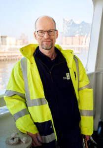 Generalsekretär MAtthias Ristau in Sicherheitsjacke bei einem Bordbesuch auf einem Schiff in Hamburg 
