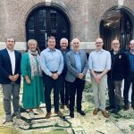 Acht Personen stehen in einem alten Gebäude auf einer Karte des Hafens. Es sind die Trustees der ICMA, eine Frau und sieben Männer