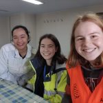 Freiwillige treffen glückliche Seefrau Links die junge Seefrau im weißem Overall, danben die beiden Freiwilligen in gelber und orangener Sicherheitskleidung