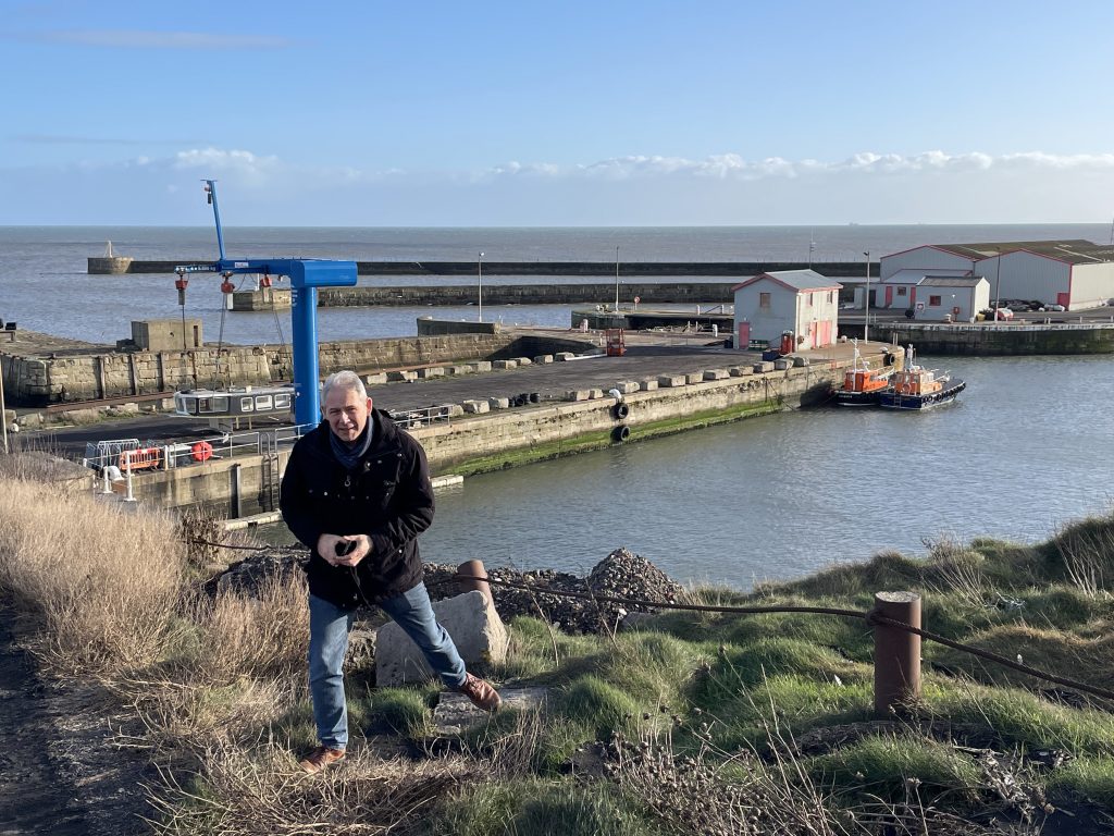 Dirk Obermann geht über ein holpriges Gelände an einem Abhang. Unten ist der Hafen Seaham mit Hafenanlagen zu sehen 