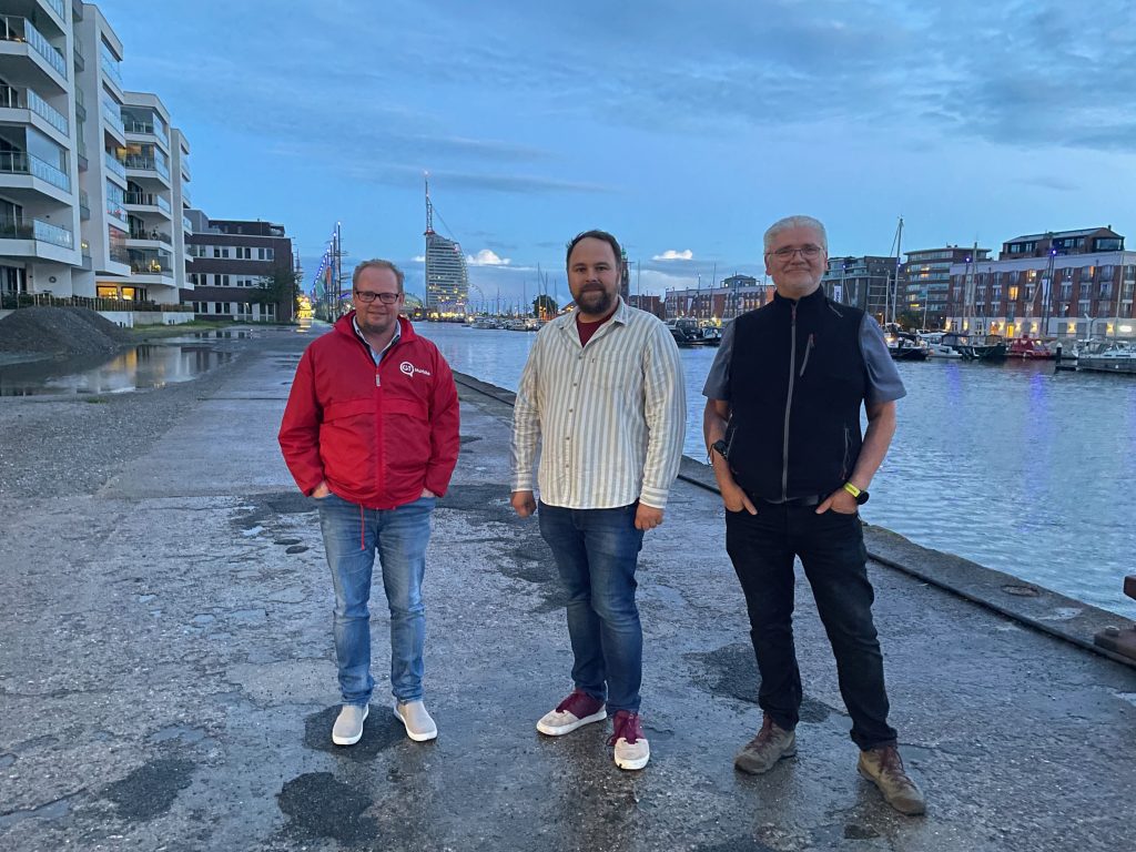 In der Abenddämmerung stehen drei Männer vor dem Hintergrund des alten Hafens von Bremerhaven