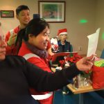 Zwei Seemänner und eine Frau schauen auf den Liederzettel und singen - im Hintergrund ist die Musikerin am Keyboard zu sehen - Freudig Weihnachtslieder singen an Bord