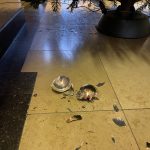 Eine goldene Weihnachtsbaumkugel aus Glas liegt zerbrochen auf dem Steinfußboden unter einem Tannenbaum - Vorweihnachtszeit
