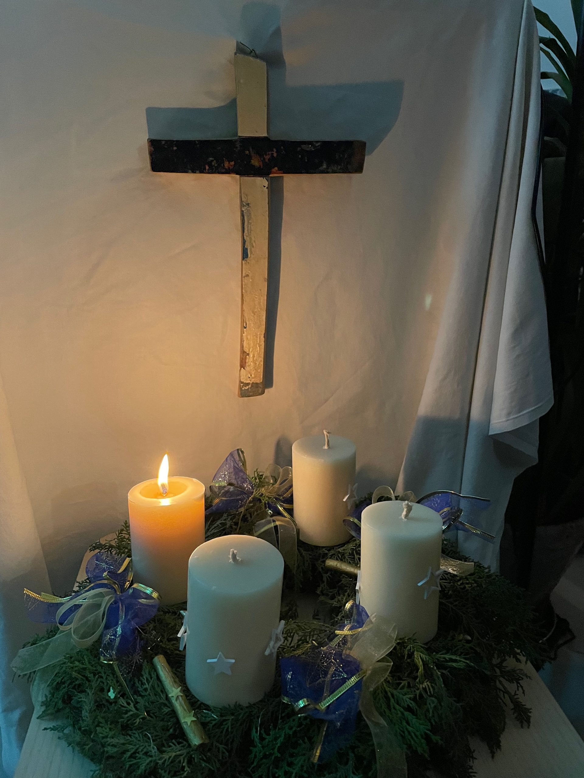 Machet die Tore Weit - Foto von Adventskranz mit weißen Kerzen. Eine brennt. Dahinter ist ein Holzkreuz an der Wand