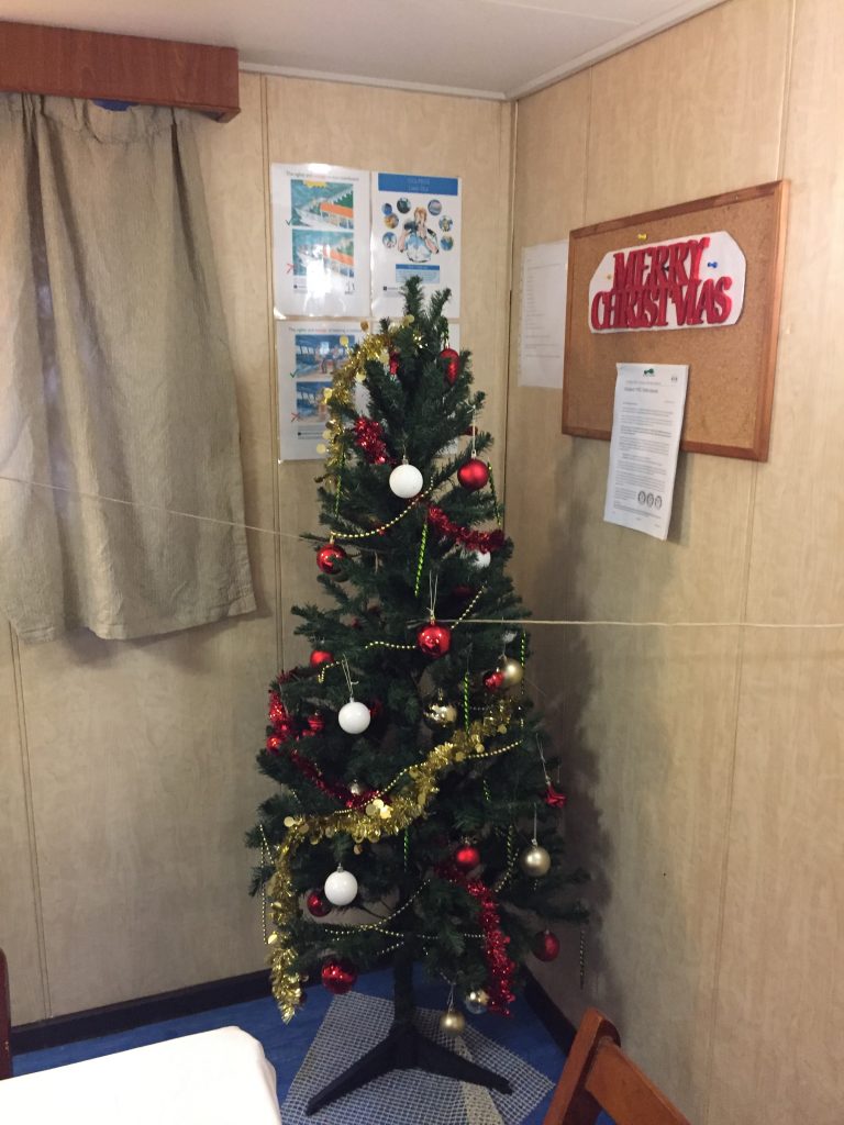 Ein Weihnachtsbaum in der Ecke eines Raumes auf einem Frachtschiff

