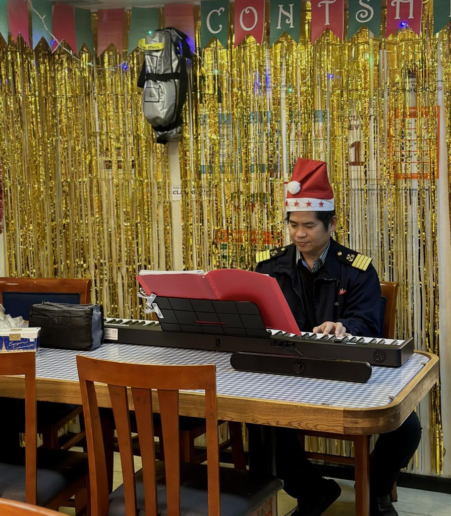 Ein Kapitän in dunkler Uniform sitzt mit Weihnachtsmütze am Keyboard und spielt