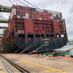 Zu sehen ist ein schwarzes Containerschiff, das viele bunte Container geladen hat. Es ist die Al Jasrah, die an den Kaianlagen im Hafen von Singapur liegt. Die Seemannsmission hat die Seeleute betreut. Sie sagt: "Rotes Meer für Seeleute lebensgefährlich."