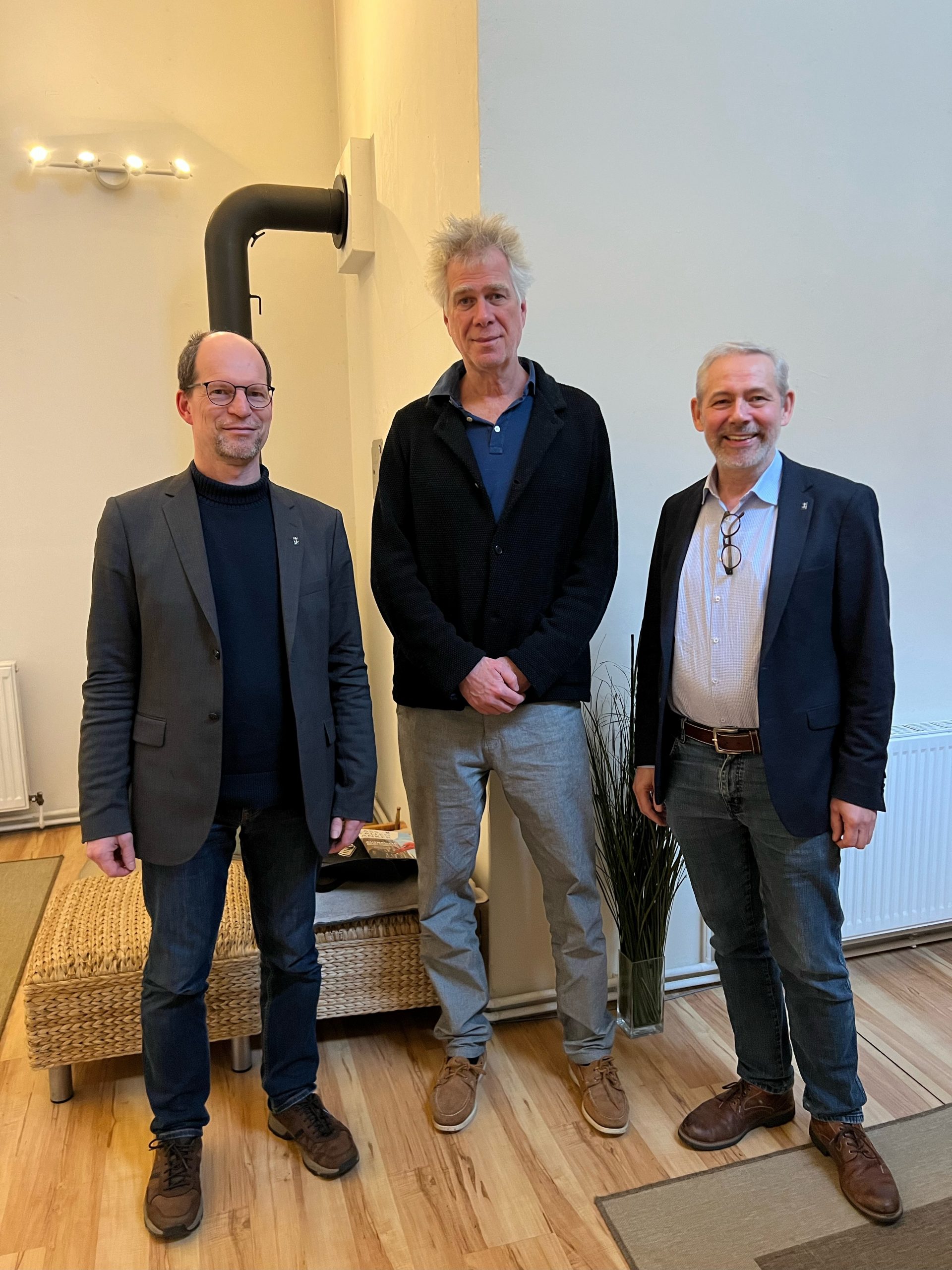 Matthias Ristau, Nikolaus Gelpke und Dirk Obermann stehen in einem Raum mit Holzfußboden vor einer weißen Wand