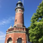 Der Leuchtturm in Kiel Holtenau - hier findet die Andacht unterm Leuchtturm während der Kieler Woche statt. Der Himmel ist blau, davon hebt sich der Leuchtturm aus roten klinkern ab.