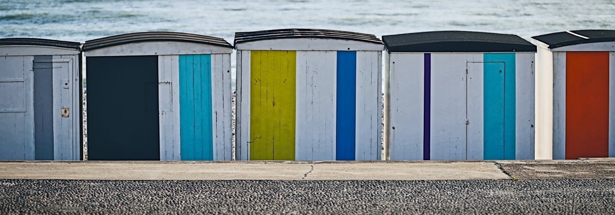 Das Foto zeigt weiß, gelb, blau, rot, türkis und schwarz angestrichene Umkleidekabinen aus Holz am Strand von Le Havre.