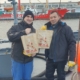 Das Foto zeigt zwei Seeleute an Bord eines Schiffes. Die beiden Männer halten Weihnachtstüten in den Händen und zeigen sie in die Kamera. Der Seemanns links im Bild trägt eine dunkle Mütze, beide tragen dunkle Arbeitskleidung. Der Seemannn rechts im Bild hat gelbe Arbeitshandschuhe an. Beide freuen sich über die Weihnachtsgeschenke der Seemannsmission Cuxhaven.