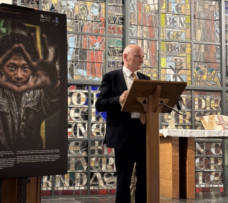 Der Deutsche Botschafter in Athen steht in der KIrche am Pult, lnks ist ein Foto von einem Seemann 