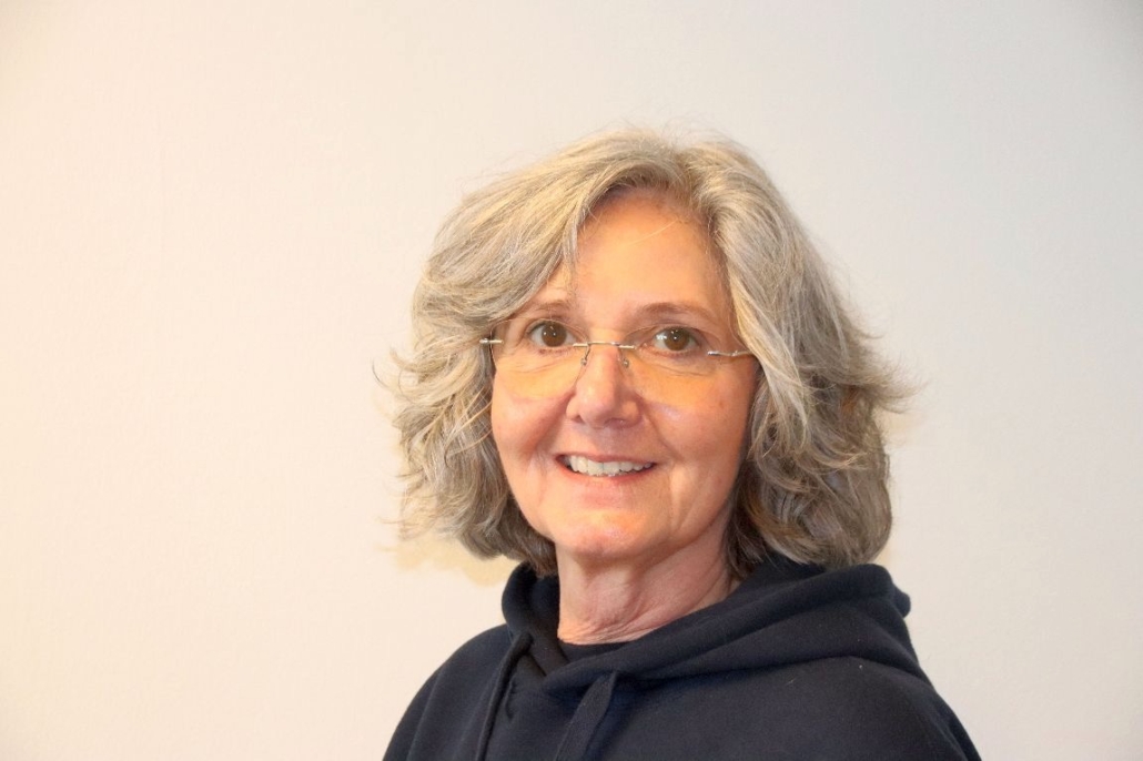 Das Foto zeigt Eliane Lafendt, die einen schwarzen Hoodie trägt, eine randlose Brille mit silbernen Bügeln und ihr mittellanges, leicht welliges, graues Haar offen trägt. Die 60-Jährige lächelt zaghaft in die Kamera.