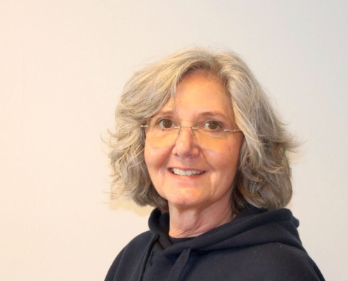 Das Foto zeigt Eliane Lafendt, die einen schwarzen Hoodie trägt, eine randlose Brille mit silbernen Bügeln und ihr mittellanges, leicht welliges, graues Haar offen trägt. Die 60-Jährige lächelt zaghaft in die Kamera.