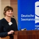 Dr. Scarlett Kleine-Kampmann spricht auf dem Symposium zum Thema Tod und Sterben an Bord. Das Foto zeigt sie hier am Rednerpult vor einem Aufsteller mit dem weiß-blauen Logo der Deutschen Seemannsmisison.