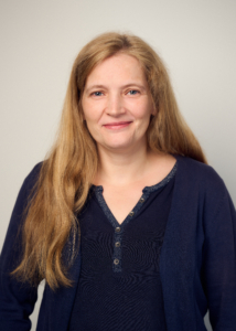 Das Portraitfoto zeigt Andrea Meenken, die den Standort der Deutschen Seemannsmission in Panama leitet. Sie trägt ihre langen blonden Haare offen, ein marineblaues, langärmliches Oberteil aus Baumwolle und lächelt freundlich in die Kamera. Sie steht vor einem beigefarbenen Hintergrund, wahrscheinlich ein Fotostudiohintergrund.