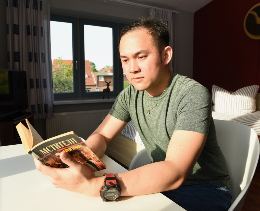 Ein philippinischer Seemann liest ein Buch. Er sitzt in einem der Übernachtungszimmer im Seemannsclub der Deutschen Seemannsmission Brunsbüttel. Die Sonne scheint in das Zimmer. Im Hintergrund ist ein Bett zu sehen.