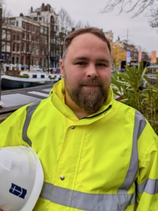 Das Foto zeigt Seemannsdiakon Thomas Kirschner, der den Standort in Amsterdam leitet. Er trägt eine neongelbe Jacke und hält einen weißen Schutzhelm in seinem rechten Arm.