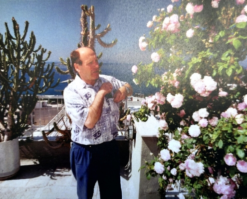 Das Foto zeigt den ehemaligen Seemannsdiakon Walter Bott auf der Terrasse des Seemannsheims in Piräus. Bott war ein begnadeter Gärtner, züchtete Rosen und ernetete jedes Jahr kiloweise Tomaten. Das Foto ist Ende der 1980er Jahre entstanden und zeitgt ihn in einem kurärmeligen weißen Hemd und langer dunkler Hose. Die Sonne scheint, im Hintergrund sind Kakteen zu sehen, die in Töpfen ebenfalls auf der Terrasse stehen.