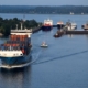 Das Foto zeigt die Schleusen in Kiel-Holtenau des Nord-Ostsee-Kanals. Vorn links im Bild sieht man ein Containerschiff mit vielen Containern in Rot-, Orange-, Grün- und Blautönen. Die Wasseroberfläche ist ruhig, zu sehen ist eine Abend- oder Morgenstimmung.