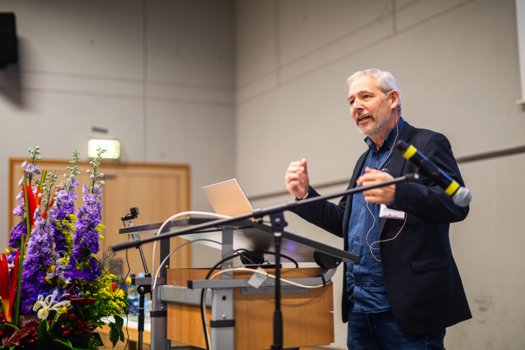 Das Foto zeigt PSNV-Koordinator Dirk Obermann von der Deutschen Seemannsmission. Er spricht über psychische Belastungen von Seeleuten bei einer Feier zu 25 Jahren Notfallseelsorge Hamburg in der Feuerwehrakademie Hamburg. Er steht am Rednerpult und gestikuliert mit seinen Händen.