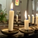 Das Foto zeigt Kerzen, die zum Gebet aufgestellt werden, etwa wenn man in einer Kirchen einem Verstobenen gedenken möchte. Mehrere weiße, schmale Kerzen brennen auf einem Metallständer im Halbkreis.