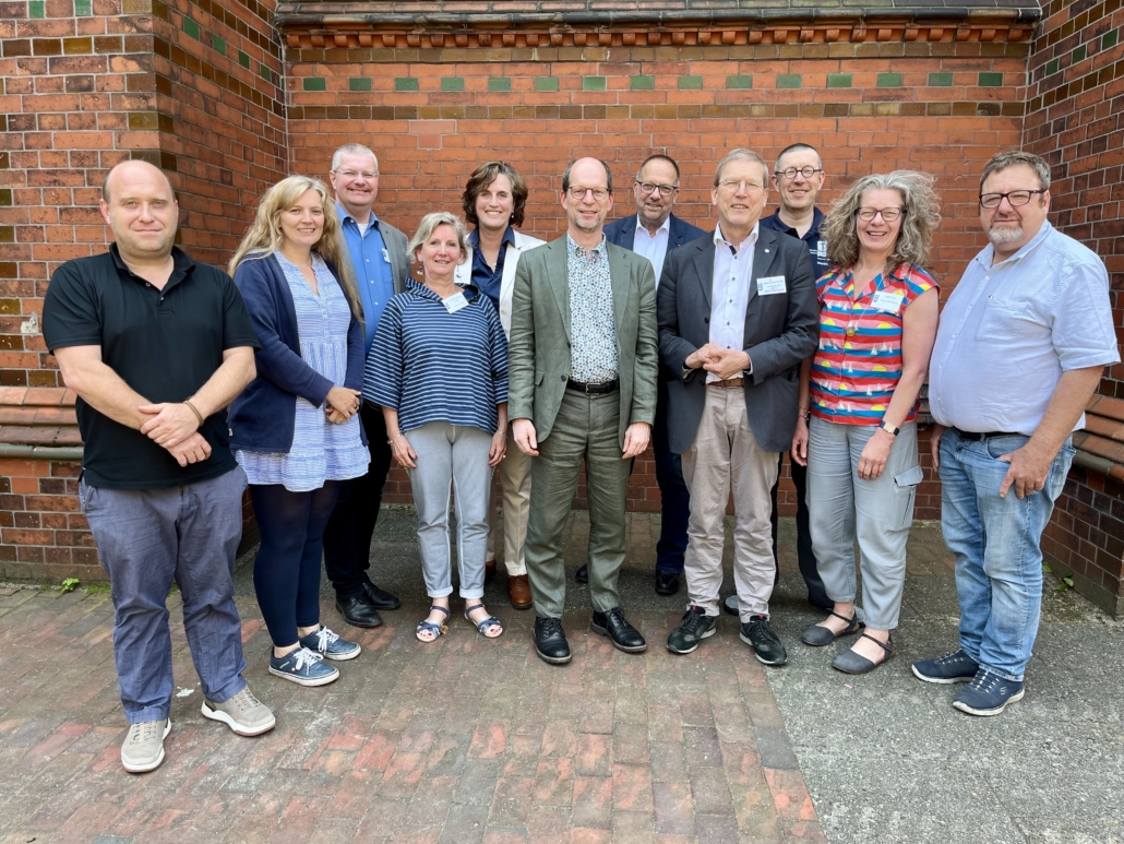 Vor einer roten Backsteinmauer steht in zwei Reihen der Ständige Ausschuss der Deutschen Seemannsmission, der im Juli 2025 neu gewählt wurde. Zu sehen sind von links nach rechts Sebastian Drabsinski, Andrea Meenken, Dirk, Silke Weißker-Voigras, Dr. Clara Schlaich, Matthias Ristau, Michael Skiba, Dr. Hans Christian Brandy, Martin Struwe, Birgit Haaks, Leon Meier