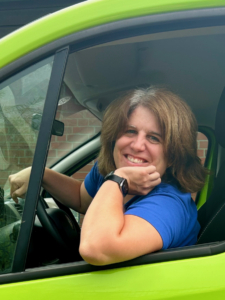Das Foto zeigt Diakonin Kerstin Schefe, die die Seemannsmission in Stade-Bützfleth leitet. Sie sitz am Steuer eines apfelgrünen Vans der Seemannsmission, hat das linke Seitenfenster heruntergefahren, stützt ihr Kinn auf ihren linken Arm und lächelt freundlich in die Kamera. Sie trägt ihr schulterlanges Haar mit grauem Ansatz offen.