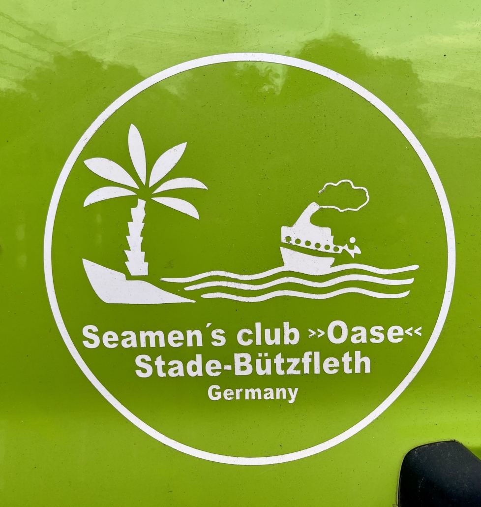 Zu sehen ist das weiße Logo auf hellgrünem Hintergrund einer Autotür des Seemannsclubs Oase in Stade-Bützfleth. Es ist ein Standort der Deutschen Seemannsmission in Niedersachsen.