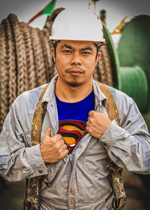 Das Foto zeigt einen jungen philippinischen Seemann, der ernst in die Kamera blickt. Auffällig ist sein blaues T-Shirt, das unter dem vermutlich ölverschmierten grauen Arbeitsoverall herausschaut, weil der Reußverschluss etwas geöffnet wurde. Es ist ein Superman-T-Shirt, das zu sehen ist. Der Fotograf heißt Aljon Manlangit, das Foto hat er "Ich bin Seemann und ich bin ein Held" genannt. Im Hintergrund sieht man eine grüne Trommel, wahrscheinlich mit einem aufgerolltem Tau oder einer dicken Kette. Der Seemann trägt einen weißen Schutzhelm auf dem Kopf. Auf seinen Schultern liegt locker ein mit weißer Farbe verschmierter Gurt, an dessen Ende Metallösen angebracht sind.