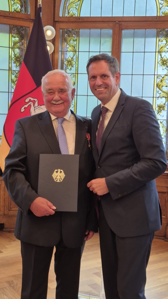 Rechts Ministerpräsidnet Olaf Lies, lnks Wilfried Adam, der den Ordner mit dem Bundesverdienstkreuz in der Hand hätl - Ehrung für Wilfrid Adam