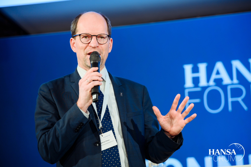 Das Foto zeigt Matthias Ristau, Generalsekretär der Deutschen Seemannsmission, mit einem Mikrofon sprechend und gestikulierend vor einem blauen Hintergrund. Er spricht auf dem 27. Hansa-Forum im Internationalen Maritimen Museum in Hamburg, wo sich die maritime Gemeinschaft zum 27. Mal trifft, vernetzt und informiert.