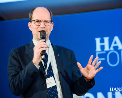 Das Foto zeigt Matthias Ristau, Generalsekretär der Deutschen Seemannsmission, mit einem Mikrofon sprechend und gestikulierend vor einem blauen Hintergrund. Er spricht auf dem 27. Hansa-Forum im Internationalen Maritimen Museum in Hamburg, wo sich die maritime Gemeinschaft zum 27. Mal trifft, vernetzt und informiert.
