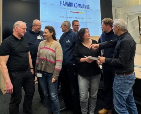 Das Foto ist ein Schnappschuss vom Treffen der Fachberater maritime PSNV beim Havariekommando in Cuxhaven, sechs Männer und zwei Frauen unterhalten sich lebhaft im Stehen vor einem Bildschirm im Inneren des Havariekommandos.