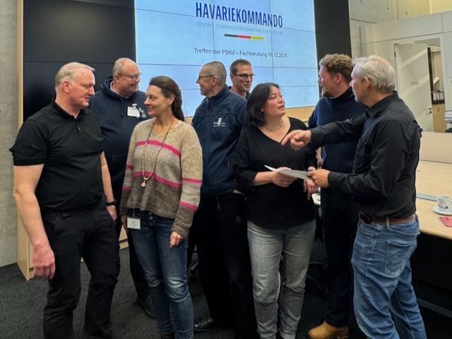 Das Foto ist ein Schnappschuss vom Treffen der Fachberater maritime PSNV beim Havariekommando in Cuxhaven, sechs Männer und zwei Frauen unterhalten sich lebhaft im Stehen vor einem Bildschirm im Inneren des Havariekommandos.