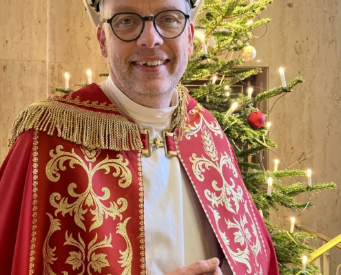 Diakon Henry Schwier, im Gewand des Heiligen Nikolaus, mit einem weißen Schutzhelm der Deutschen Seemannsmission vor einem festlich geschmückten Weihnachtsbaum.
