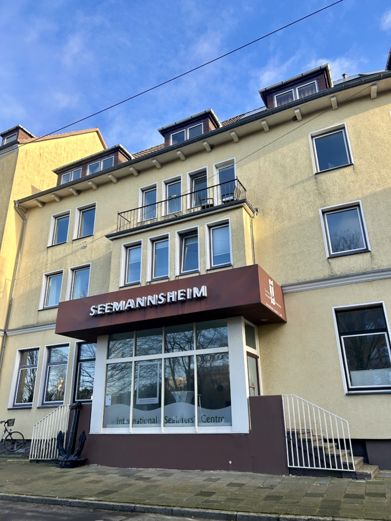 Das Foto zeigt das Seemannshotel Portside in der Schifferstraße 51 in Bremerhaven. Das Haus mit Übernachtungsmöglichkeiten und Aufenthaltsräumen für Seeleute wird nach 125 Jahren zum Ende des Jahres 2025 geschlossen. Die Fassage erstrahlt in einem freundlichen Gelb. Über dem Eingang prangt der Schriftzug "Seemannsheim" in großen weißen Lettern.