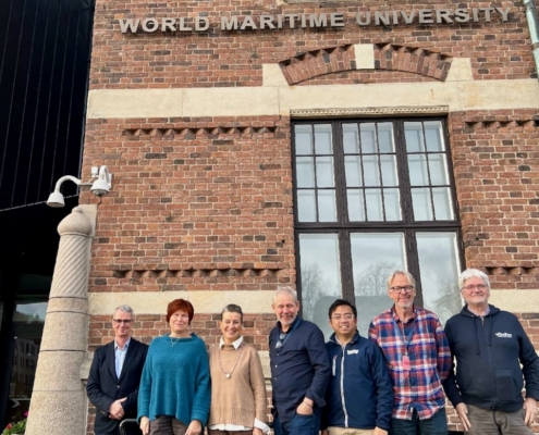 Das Foto zeigt die Akteure des neuen Netzwerks rund um maritime PSNV. Das bedeutet Psychosoziale Notfallversorgung. Vier Akteure kümmern sich im westeuropäischen Raum um Seeleute, die World Maritime University (WMU) im schwedischen Malmö ist der fünfte Kooperationspartner. Die sieben Menschen stehen vor dem Gebäude der WMU in Malmö.