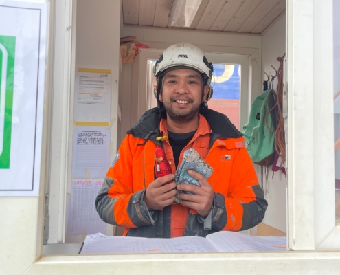 Das Foto zeigt einen philippinischen Seemann in Arbeitsoverall mit weißem Schutzhelm auf dem Kopf. Der junge Mann hölt einen Schokoladen-Weihnachtsmann und ein paar selbstgestrickte Socken in den Händen. Er freut sich und lächelt in die Kamera.