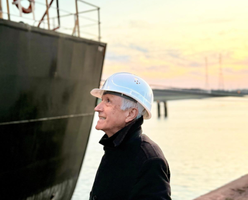 Winfried Schumann, ehemaliger Kapitän und nun im Ruhestand, steht vor einem Massengutfrachter an der Kaikante im Hafen von Bremen.