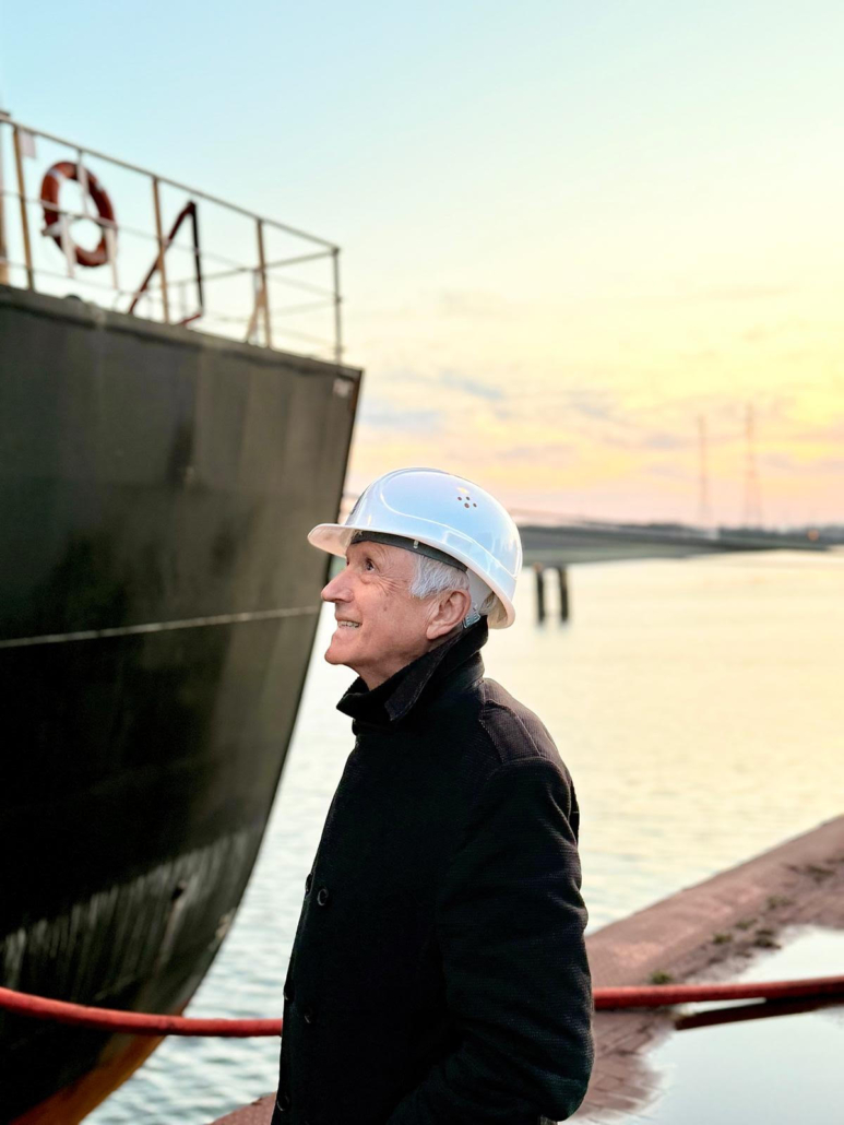 Winfried Schumann, ehemaliger Kapitän und nun im Ruhestand, steht vor einem Massengutfrachter an der Kaikante im Hafen von Bremen.