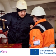 Das Bild setzt sich zusammen aus einem Foto von einem Seemann, der sich an Bord eines Schiffes mit einem Mitarbeiter der Deutschen Seemannsmission unterhält. Im unteren Drittel sind links der in hellblau und lila gehaltene Schriftzug des EU-Projektes Sea Care zu sehen. Rechts davon ist die blaue EU-Flagge mit zwölf goldenen Sternen zu sehen. Auf Englisch ist zu lesen, dass das Projekt von der EU mitfinanziert wurde.