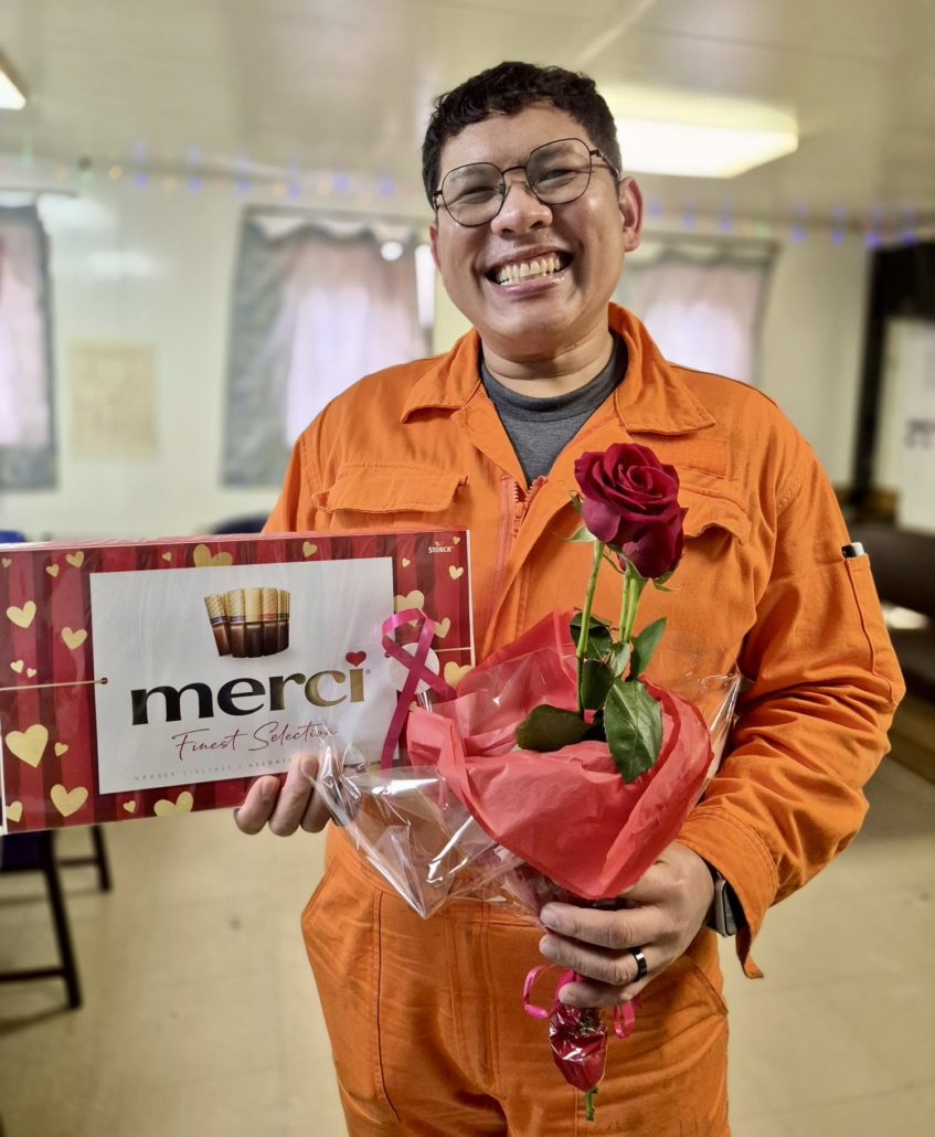 Grüße zum Valentinstag an Bord eines Schiffes im Hafen von Le Havre. Ein philippinischer Seemann hält eine Packung Schokoalde und eine rote Rose lächelnd in de Kamera.