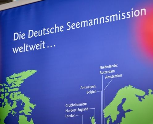 Das Symbolfoto zeigt einen Ausschnitt einer Weltkarte mit den Standorten der Deutschen Seemannsmission. Die Karte ist in Dunkelblau gehalten, mit weißer Schrift. Die Umrisse der Kontinente sind in einem hellen Grün gehalten.