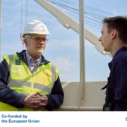 Das Fot zeigt Seemannspastor und Stationsleiter Marc Schippers (li.) mit weißem Schutzhelm und neopngelber Warnweste an Bord eines Schiffes im Hafen von Antwerpen. Er ist im Gespräch mit einem jungen Seemann. Der Mann trägt einen dunkelblauen Arbeitsoverall. Schippers hört dem jungen Seemann aufmerksam zu. Am unteren Rand stehen in einem weißen Kästchen das Logo der EU, mit einem Hinweis, dass das Projekt von der EU gefördert ist und das Sea Care-Logo in Blau-Magenta.